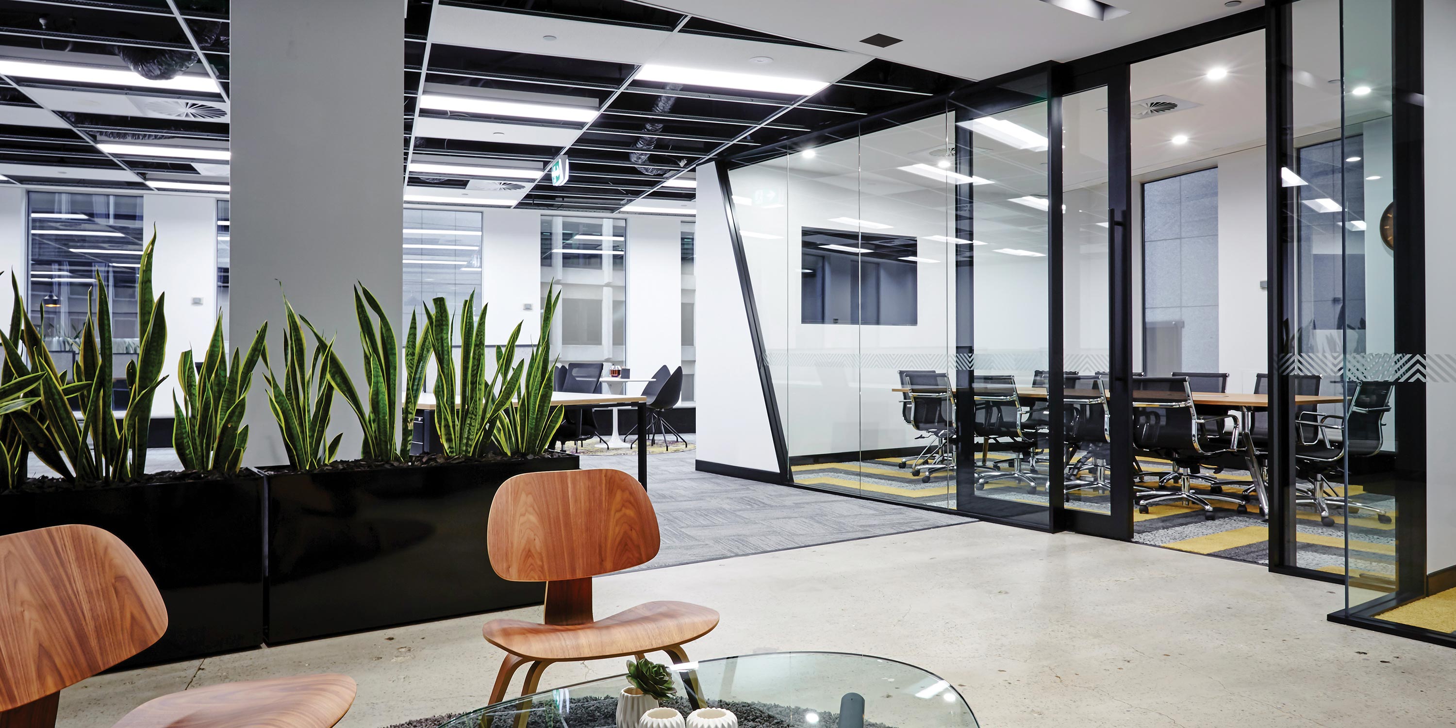 Open office space with glass meeting rooms, plants, and modern furniture