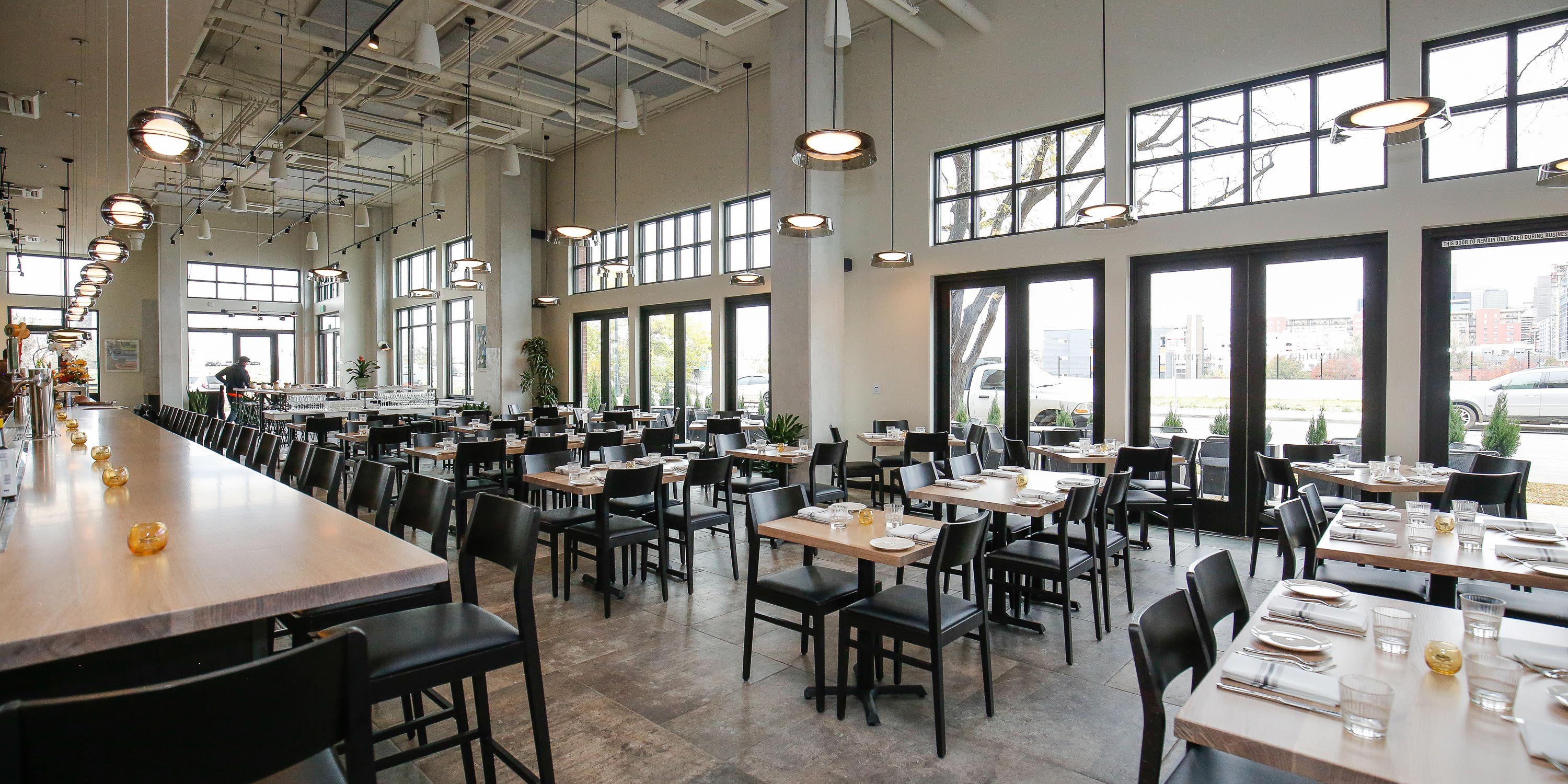 Bright restaurant interior with rows of tables, bar seating, and large windows