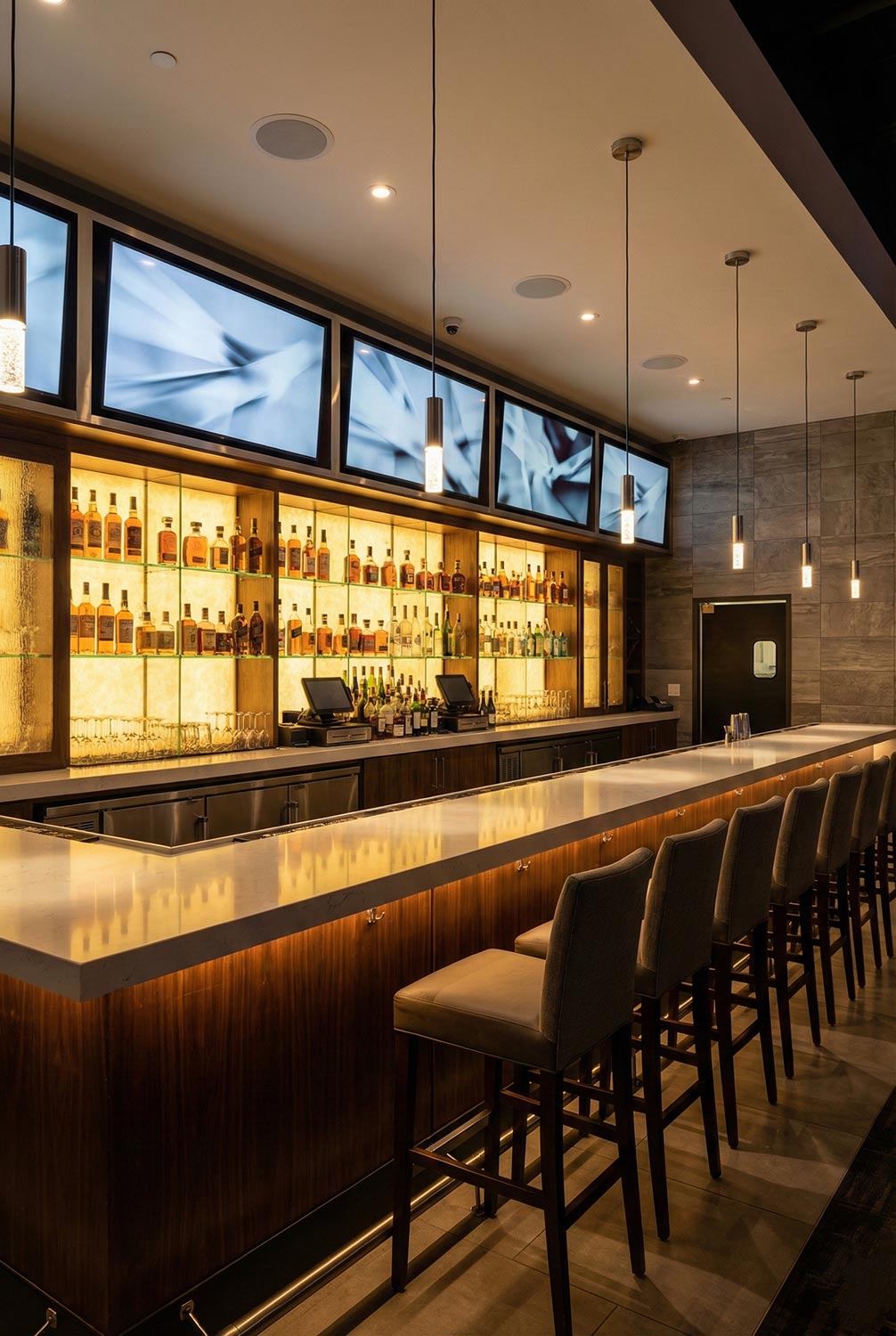 Modern bar with long counter, pendant lights, and multiple screens above