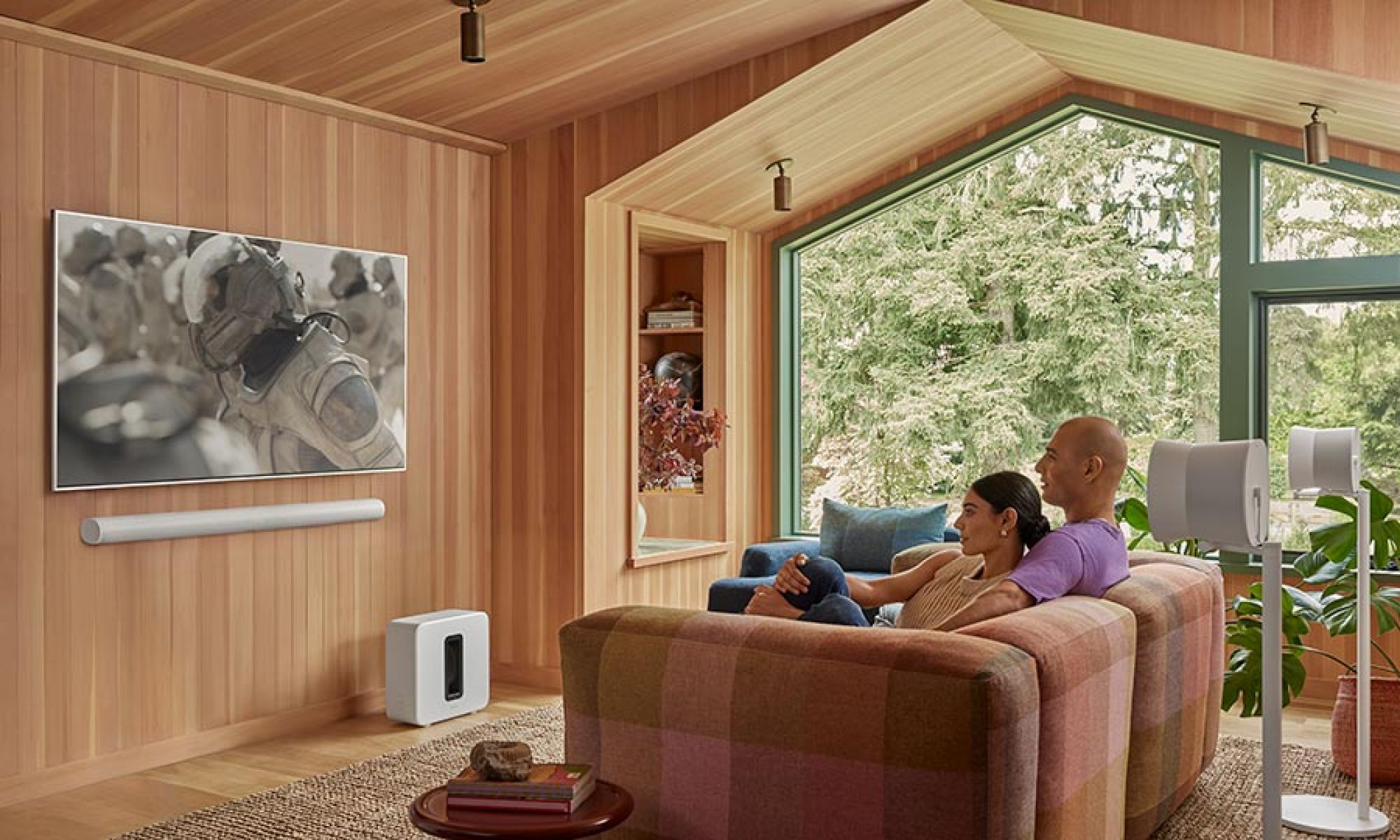 Couple watching television with soundbar and speakers in a wood paneled living room